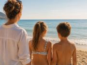 Madre con un bambino e una bambina sulla spiaggia osservati di spalle mentre guardano il mare. Immagine che rappresenta l'attenzione ai primi segnali della scoliosi durante la crescita.