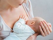 Madre che allatta il proprio neonato tenendolo tra le braccia in un momento di contatto e cura durante l’allattamento.