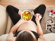 donna in gravidanza con scodella e insalata nello sfondo ecografie e scarpine da bimbo