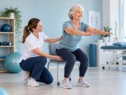 Donna anziana esegue un esercizio terapeutico assistita da una professionista in un ambiente riabilitativo.