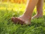 Primo piano di piedi nudi che camminano sull’erba illuminata dalla luce naturale del sole, in un contesto rilassante e legato al benessere e al movimento quotidiano.